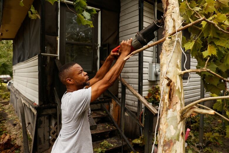 A man uses a saw to cut a tree damaged by the storm