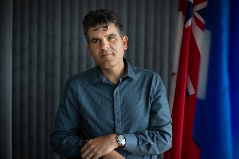 A man stands and looks off camera with flags behind him.