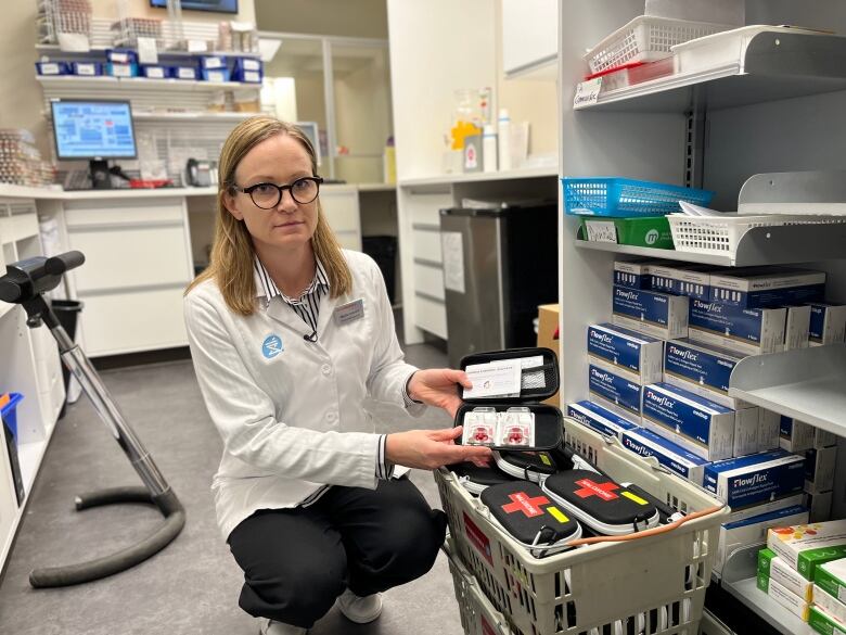 A pharmacist kneels down and opens one of many naloxone kits in the pharmacy. 