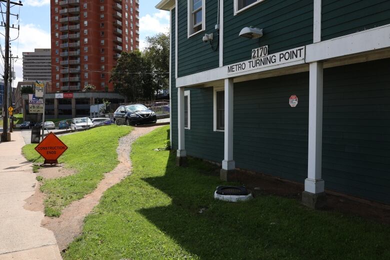 A green homeless shelter with high rise buildings and businesses in the background. 