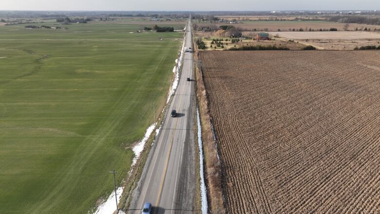 A drone shot shows a road dividing between farm land and green lands. 