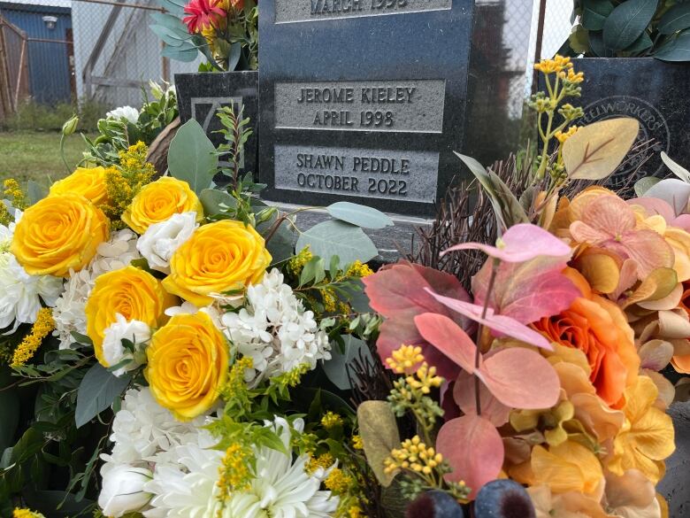 A memorial stone with name Shawn Peddled engraved into it, surrounded by flowers.