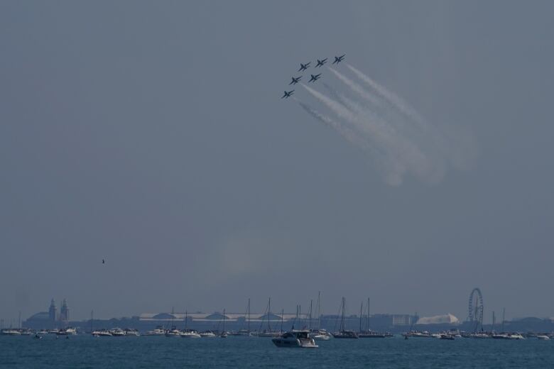 Six U.S. air force Thunderbirds flying in the sky with boaters along the shore of Lake Michigan.