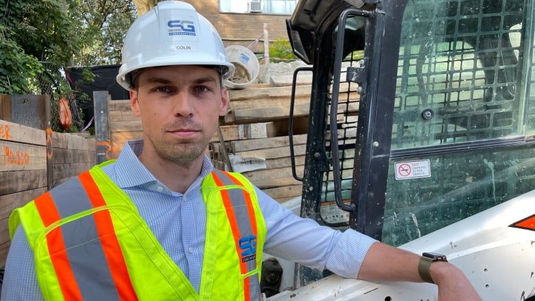 A construction manager wearing a hardhat and fluorescent vest is shown at a building site.