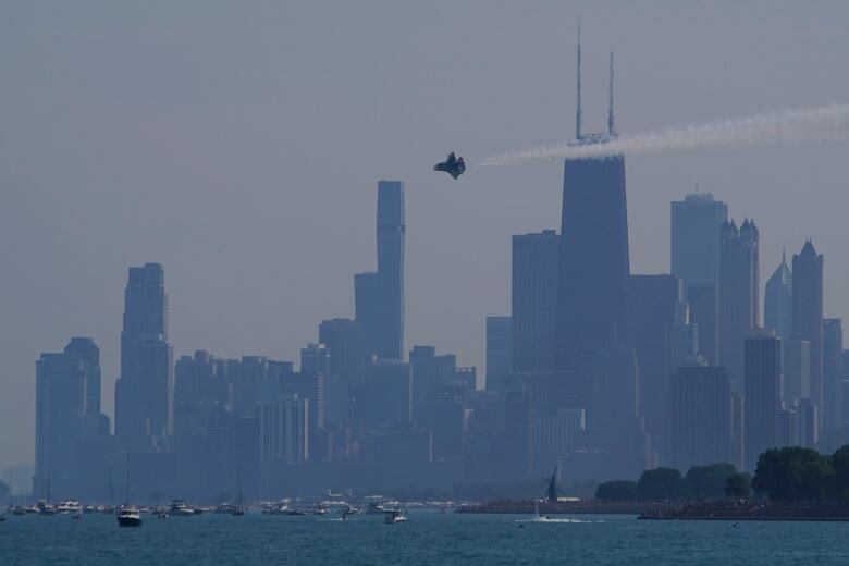 A U.S. Air Force Thunderbird flying with Chicago's skyline in the distance and boaters along the shore of Lake Michigan.