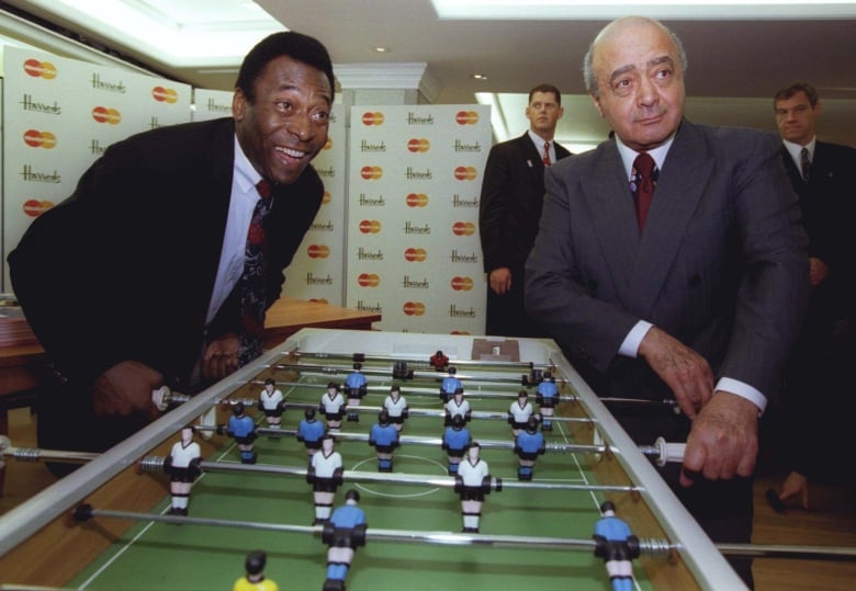 Two people pose for photos while playing foosball.