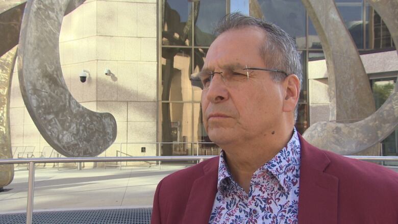 A man wearing glasses and a suit jacket stands outside a building.