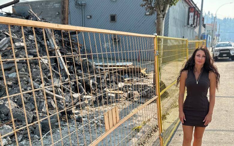 A woman stands next to a pile of debris.