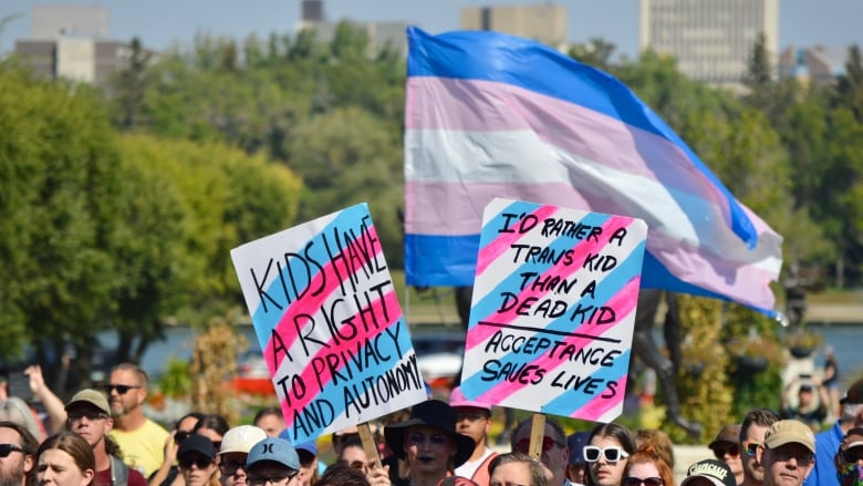 Two signs in the air above a crowd of people. One reads Kids have a right to privacy and autonomy. The second read I'd rather a trans kid than a dead kid, acceptance saves lives 