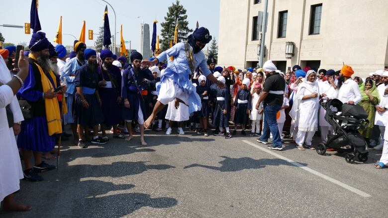 A man wearing traditional Sikh clothing jumps in front of a crowd.