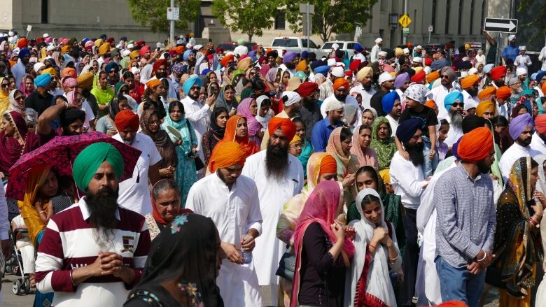 A crowd of people traditional Sikh clothing walk down a street.