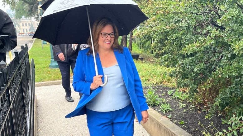 A woman in a blue suit holds an umbrella while walking down a concrete path.