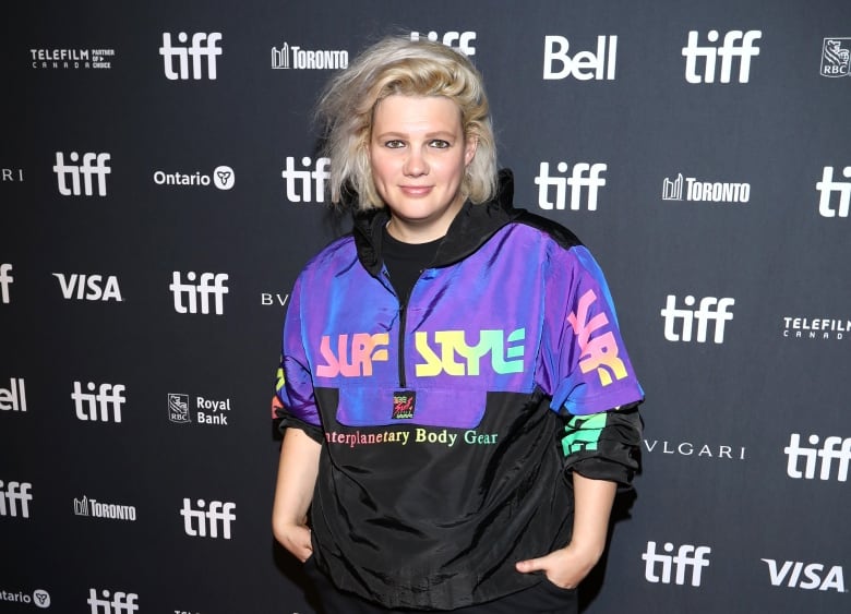 D.W. Waterson poses for a photo on the red carpet at the TIFF press conference against a black-and-white step and repeat.