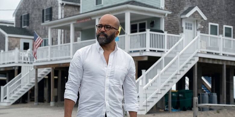 Still from American Fiction. Pictured: actor Jeffrey Wright, a bald Black man with a close beard wearing dark-framed glasses and a white button-up shirt, walks at daytime. Tall houses appear behind him.