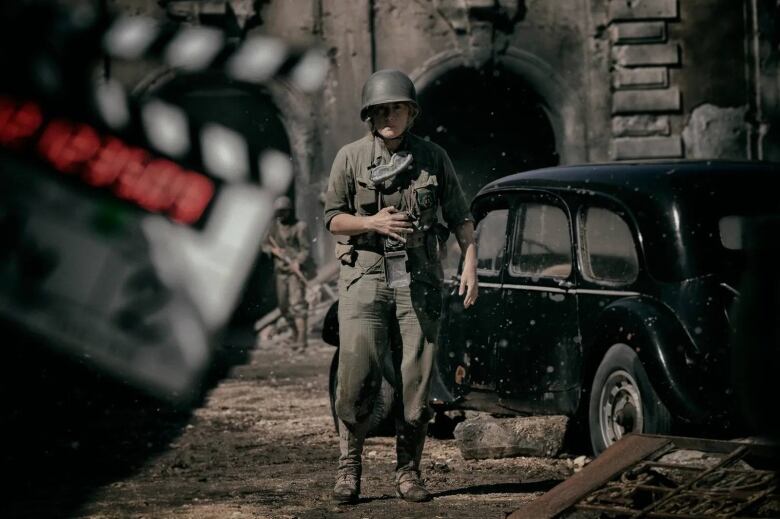 Behind-the-scenes image from Lee. On a set resembling a devastated European street during the Second World War, Kate Winslet stands at centre, costumed in military dress from her hard helmet to dark green fatigues. She is in character as photographer Lee Miller. In the foreground, a clapboard is visible, suggesting this is a film set.