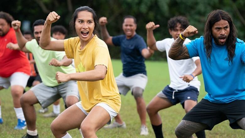 Still from Next Goal Wins. Rows of soccer players practice. They squat and appear to yell.