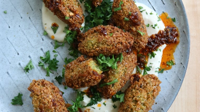 A plate of falafel with a dip and fresh herbs.