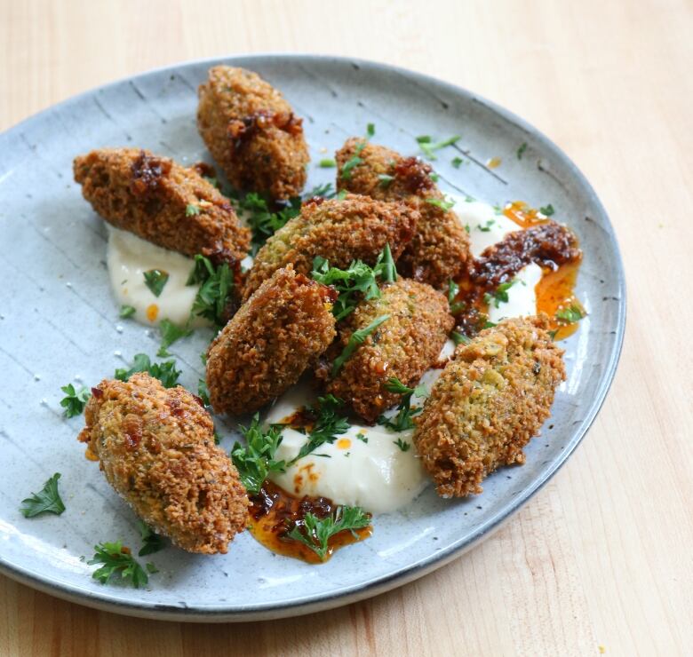 Falafel on a plate with dip and fresh herbs.