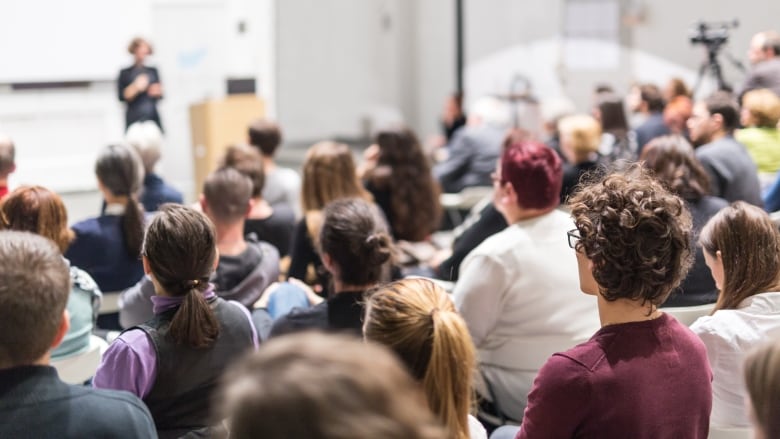 Female speaker giving presentation in lecture hall at university workshop. Audience in conference hall. Rear view of unrecognized participant in audience. Scientific conference event.