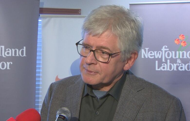 A man with grey hair and glasses stands in front of a backdrop that says Newfoundland and Labrador.