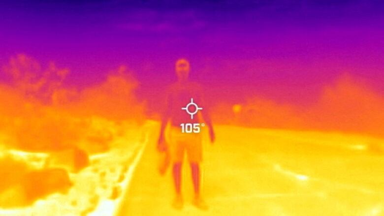 Rainbow coloured infrared image of a man standing in a park with grass that is a bit cooler