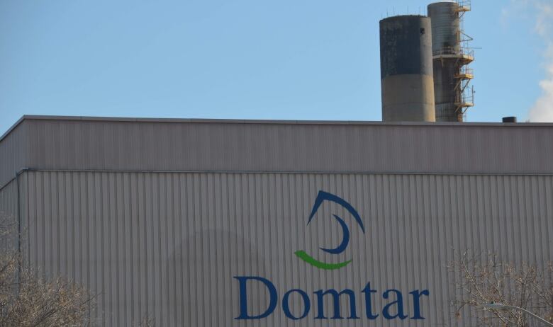 A large grey wall, with the word 'Domtar' and smokestacks on the top 