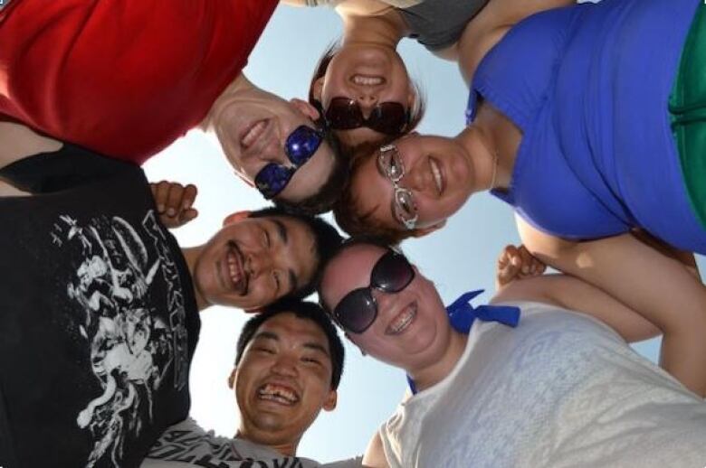 a group of Inuit students are pictured from below in a circle smiling down at the camera.