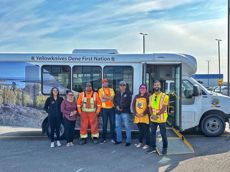 a group stands in front of a small bus.