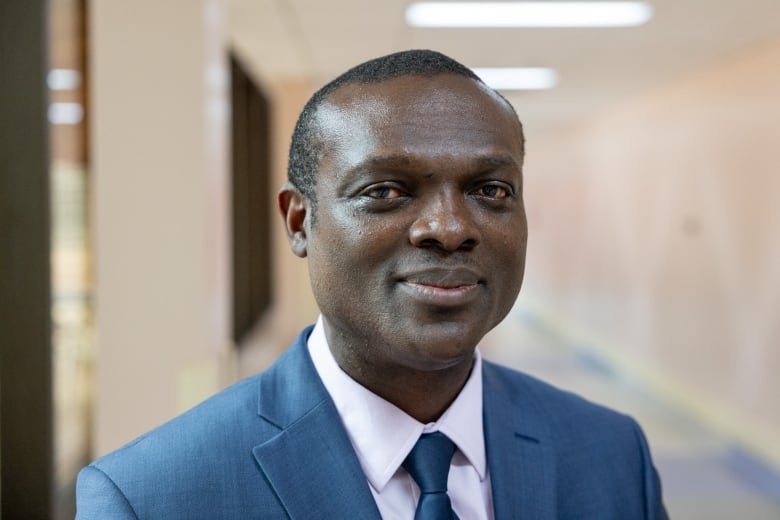 A man is shown in the corridor of a hospital in a white shirt and blue suit and tie.