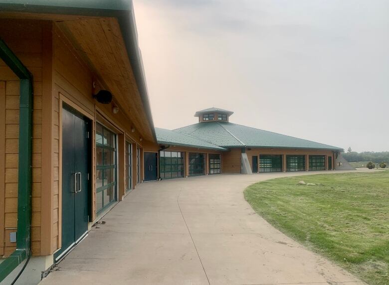 Large wooden building with green roof a trim in the middle of a new green space. 