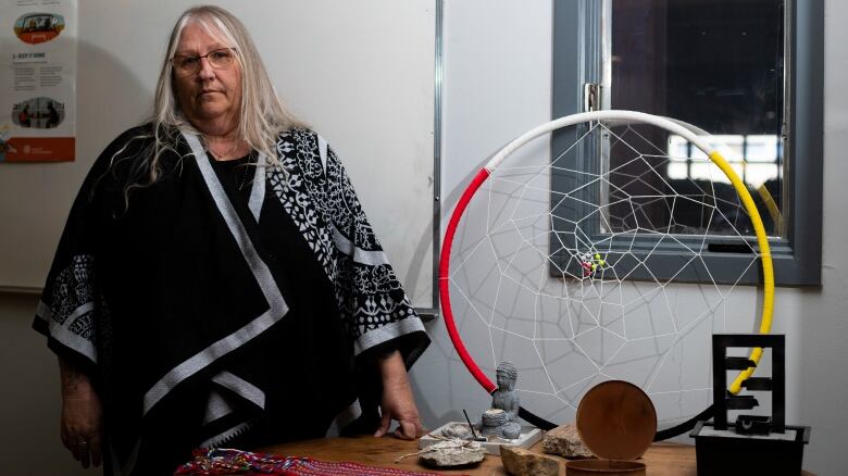 A woman stands looking serious by a medicine wheel.