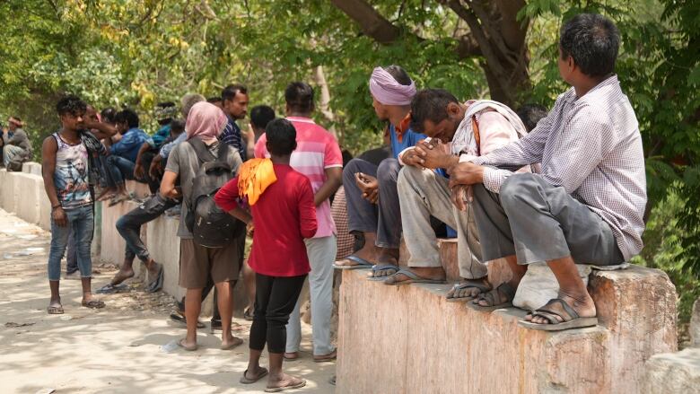 A group of men sit and gather on a short wall under the midday sun in New Delhi, India.