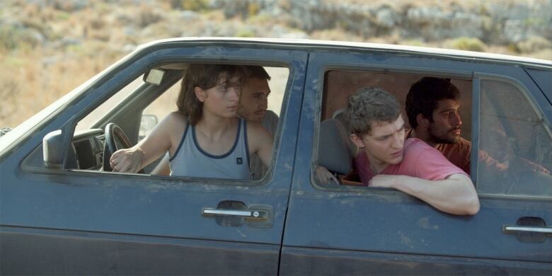 Four young people sit in the front and back seats of a black car, all looking out the back window.