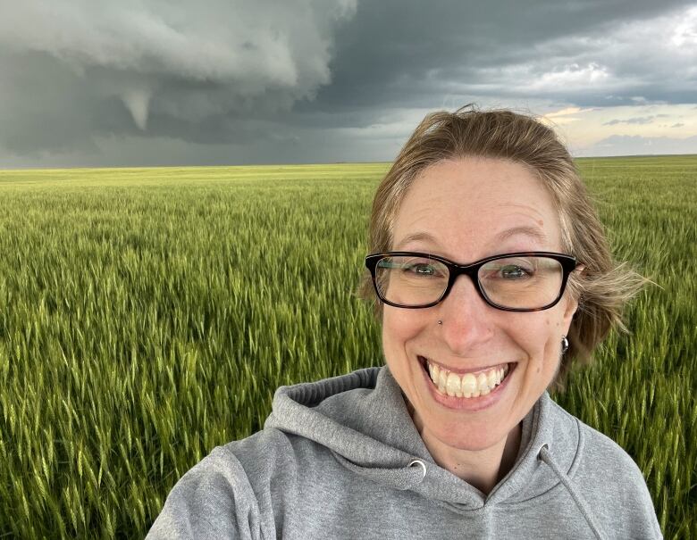 Smiling woman standing in a wheat field with a tornado behind her.