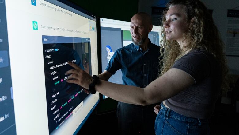 A man and woman stand in front of a large computer screen in a darkened room.