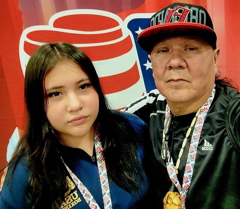 An Indigenous girl and man in front of a red, white and blue backdrop 