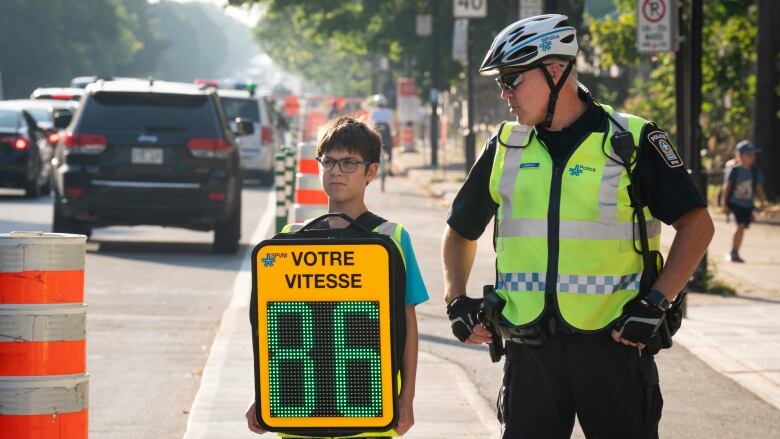 Young boy holds backpack in front of him, the number 86 lights up. Police officer beside him.