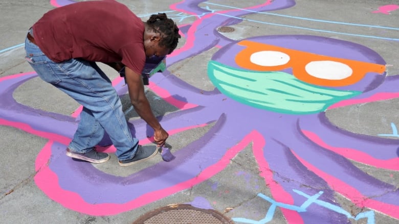 A person paints a large purple, cartoonish octopus on a city street.