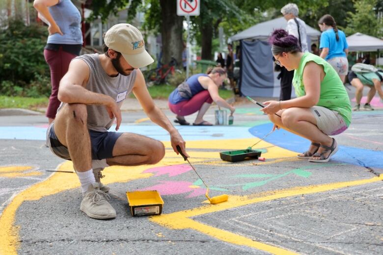 Several people are seen painting a colourful mural on a road.