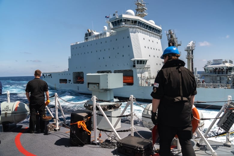 Sailors on deck look out toward a large white ship that has moved itself to be in close proximity. 