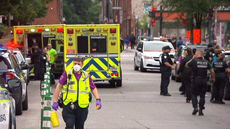 A paramedic looks up to the camera. Several police officers and paramedics with ambulances occupy a cordoned-off street.