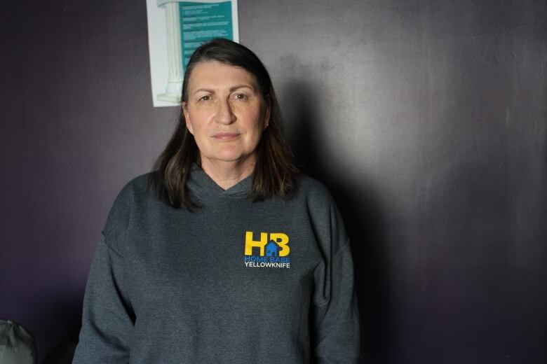 A woman wearing a grey sweatshirt stands in front of a wall painted purple.