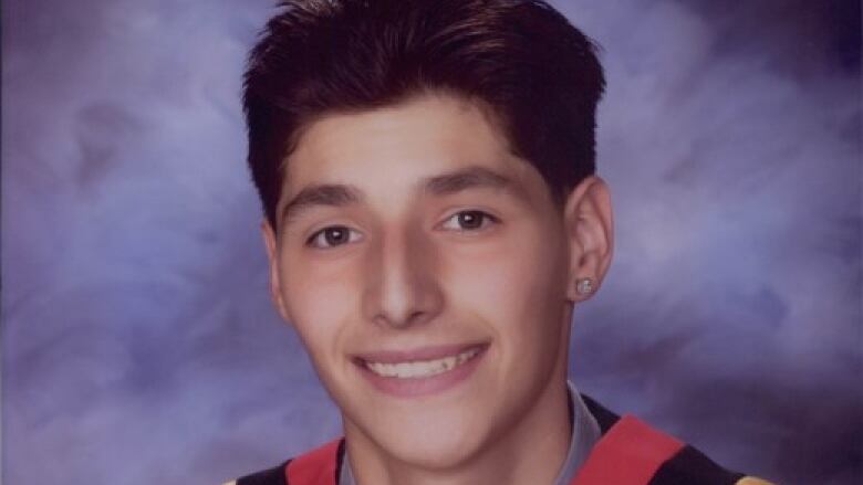 A young man poses in a graduation gown.