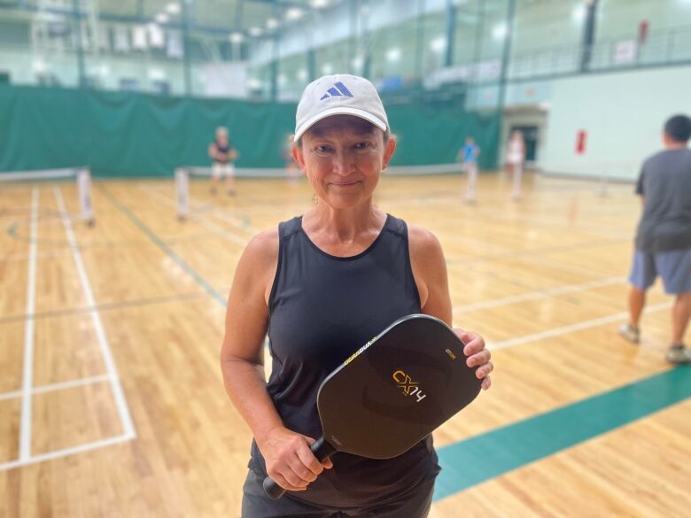 A woman holds a pickleball racquet next to a court 