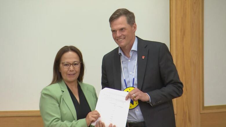 Two people standing, holding a piece of paper. 