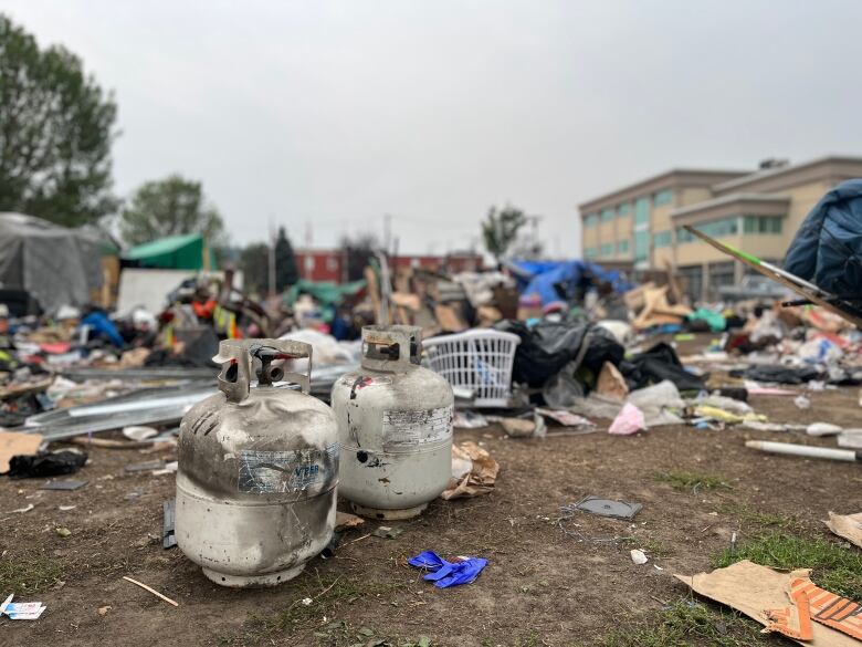 Two propane tanks in front of debris at an encampment.