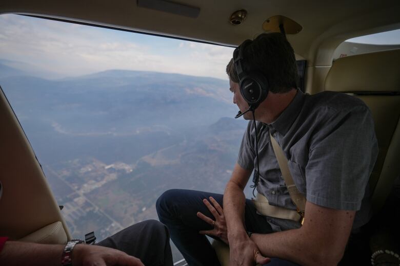 A white man looks outside a helicopter window at burnt landscape.