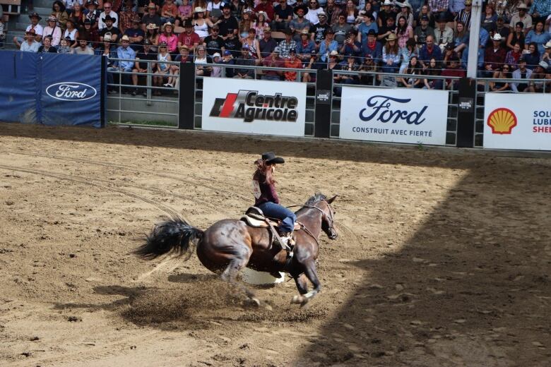 A woman rides a horse around a barrel during a competition in a rodeo.