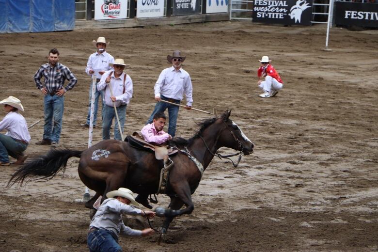 A man tries to pull himself onto a horse as it gallops. His teammate jumps off the horse and onto the ground. 