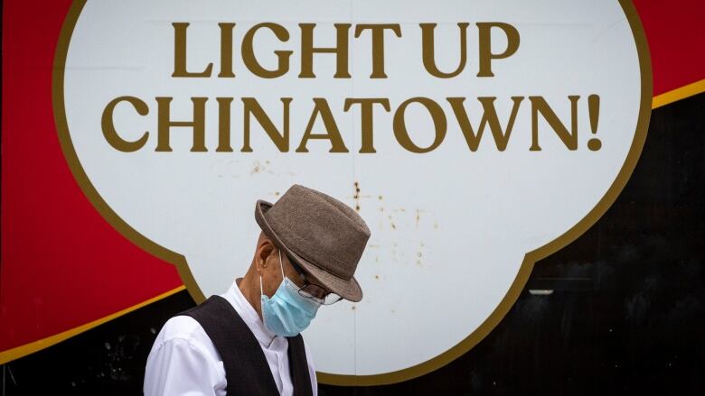 A man wearing a face mask walks past a sign that reads 'Light up Chinatown!'